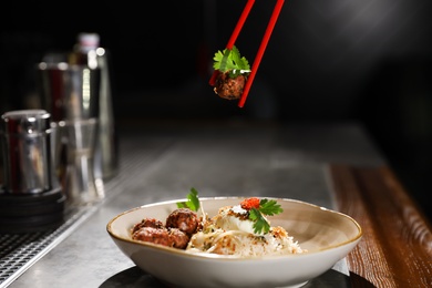 Photo of Chopsticks with meat ball over plate of rice on table indoors