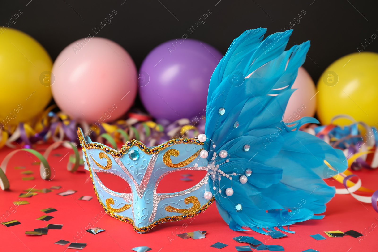 Photo of Beautiful carnival mask and party decor on red table, closeup