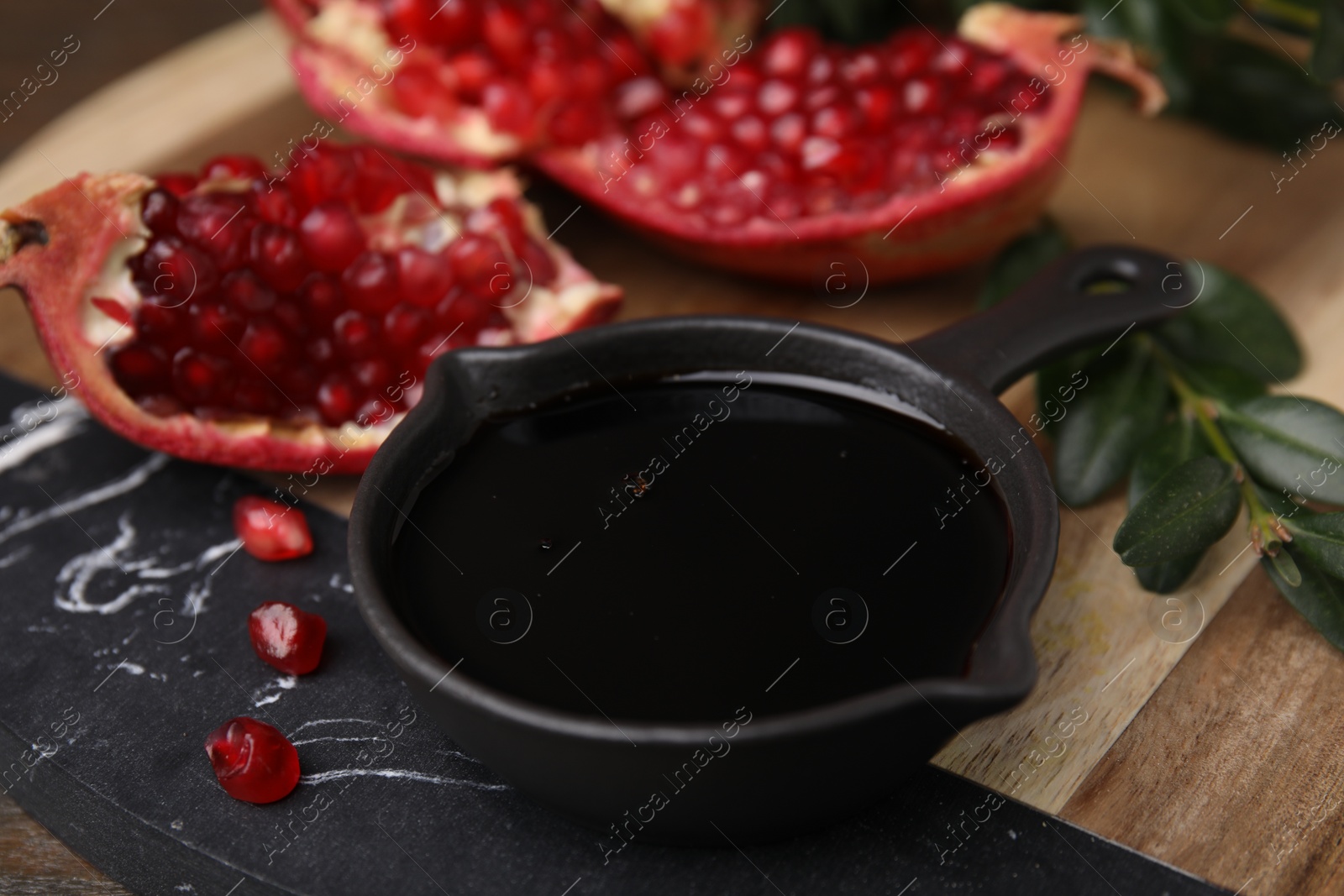 Photo of Tasty pomegranate sauce in bowl, branch and fruit on table, closeup