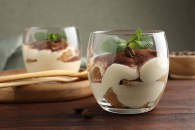 Photo of Delicious tiramisu in glasses, mint leaves and coffee beans on wooden table