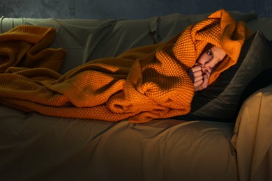 Photo of Little girl hiding from monster in blanket on sofa at night