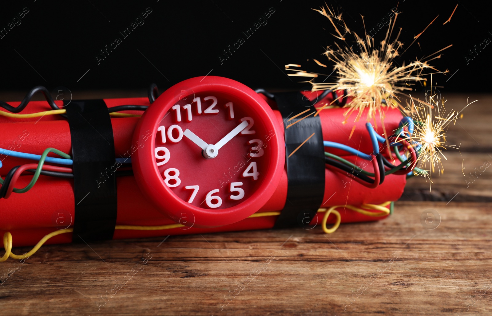 Image of Dynamite time bomb with burning wires on wooden table, closeup