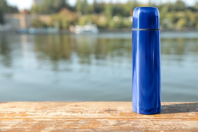 Photo of Modern blue thermos on wooden surface near river. Space for text