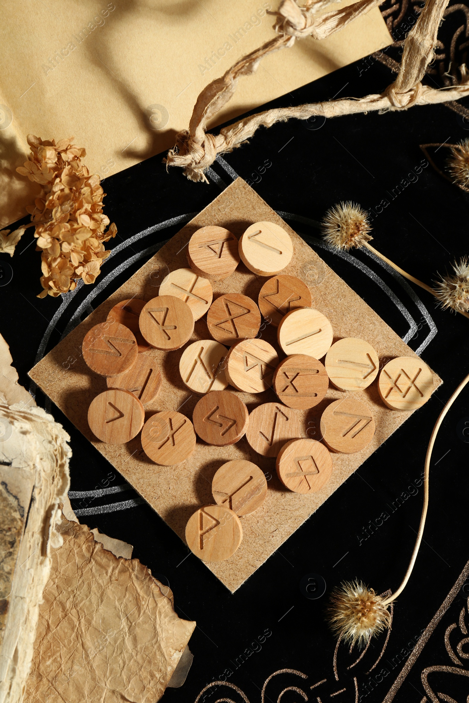 Photo of Many wooden runes, old books and dried flowers on divination mat, flat lay