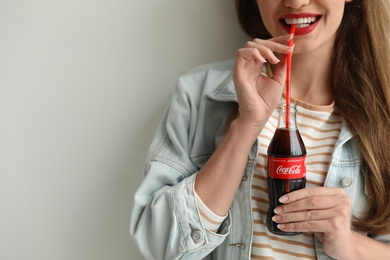 Photo of MYKOLAIV, UKRAINE - NOVEMBER 28, 2018: Young woman with bottle of Coca-Cola on light background, closeup. Space for text