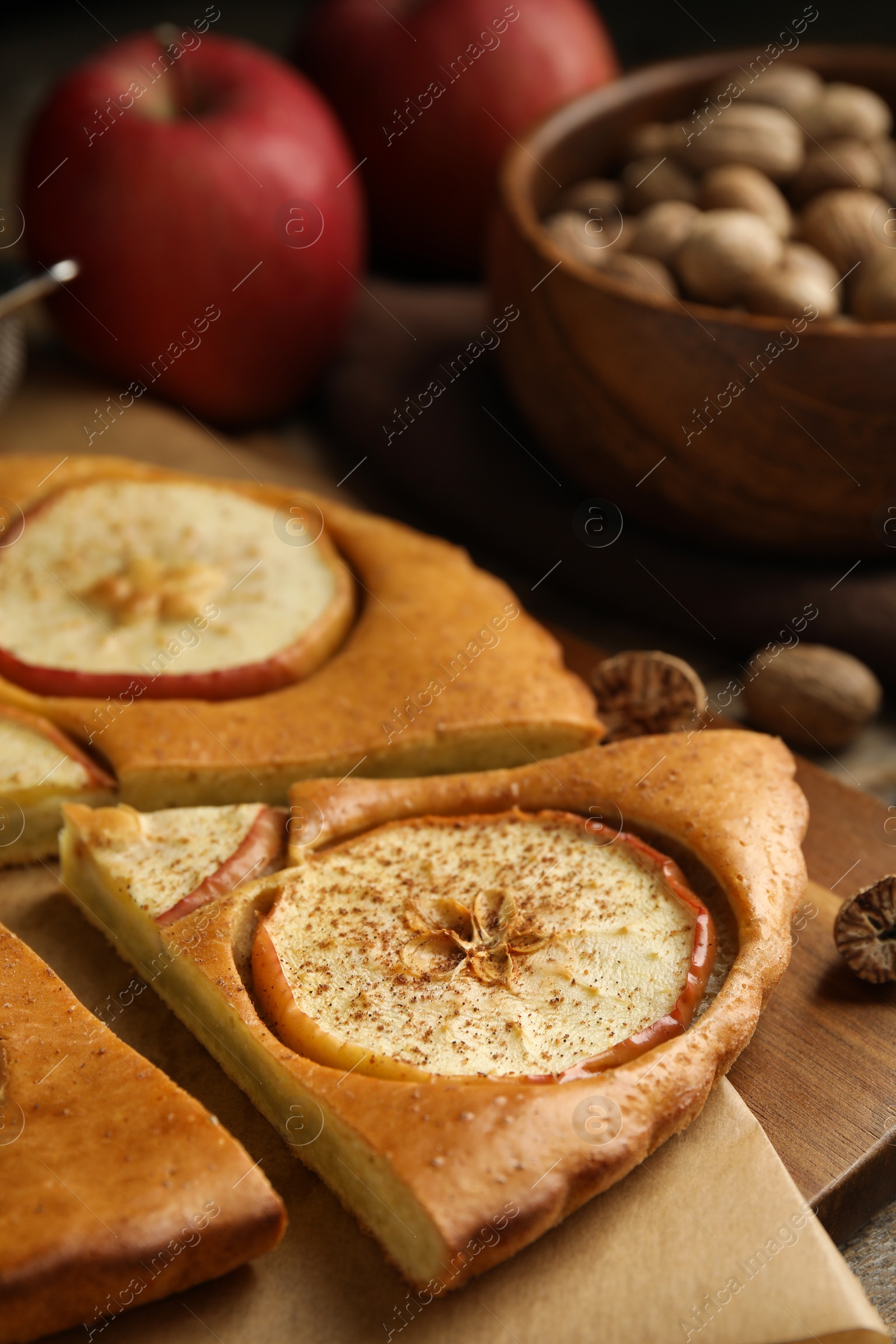 Photo of Nutmeg seeds and tasty apple pie on wooden board, closeup