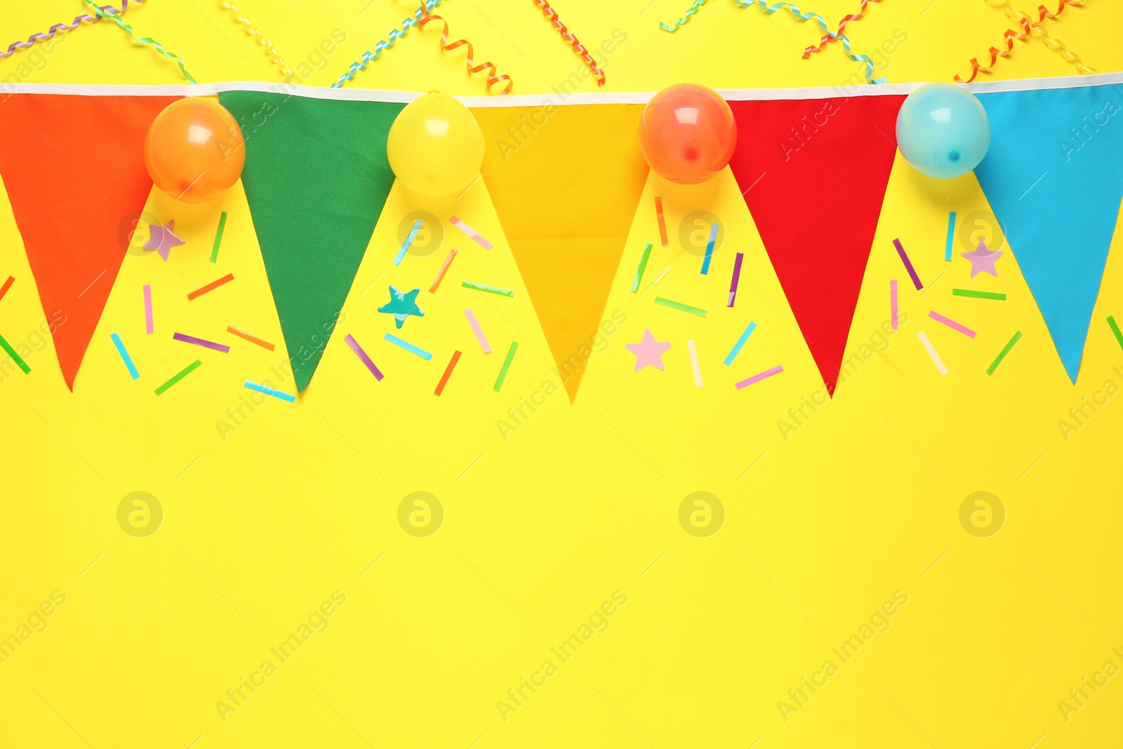 Photo of Bunting with colorful triangular flags and other festive decor on yellow background, flat lay. Space for text