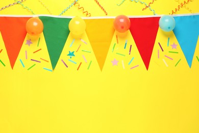 Photo of Bunting with colorful triangular flags and other festive decor on yellow background, flat lay. Space for text