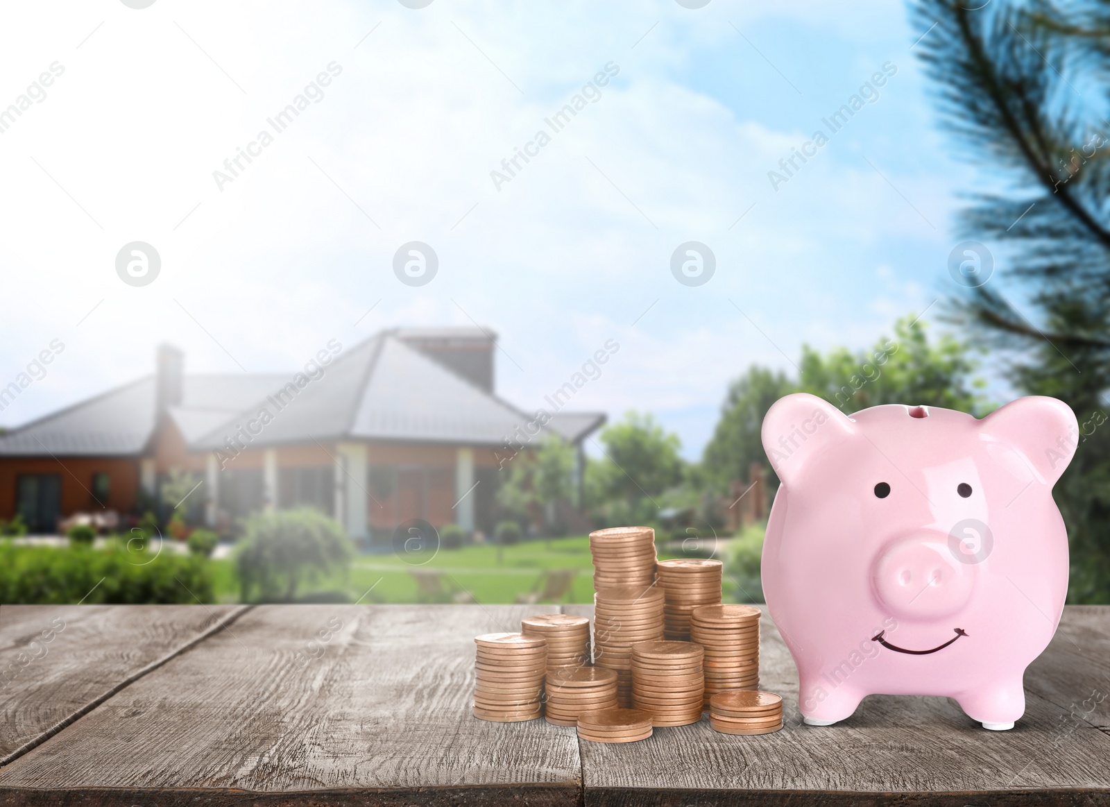 Image of Piggy bank and stacked coins on wooden surface and blurred view of beautiful house, space for text. Mortgage concept