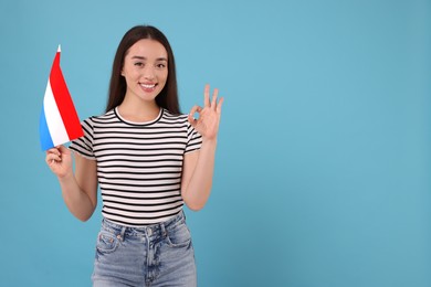 Photo of Young woman with flag of Netherlands showing ok gesture on light blue background, space for text