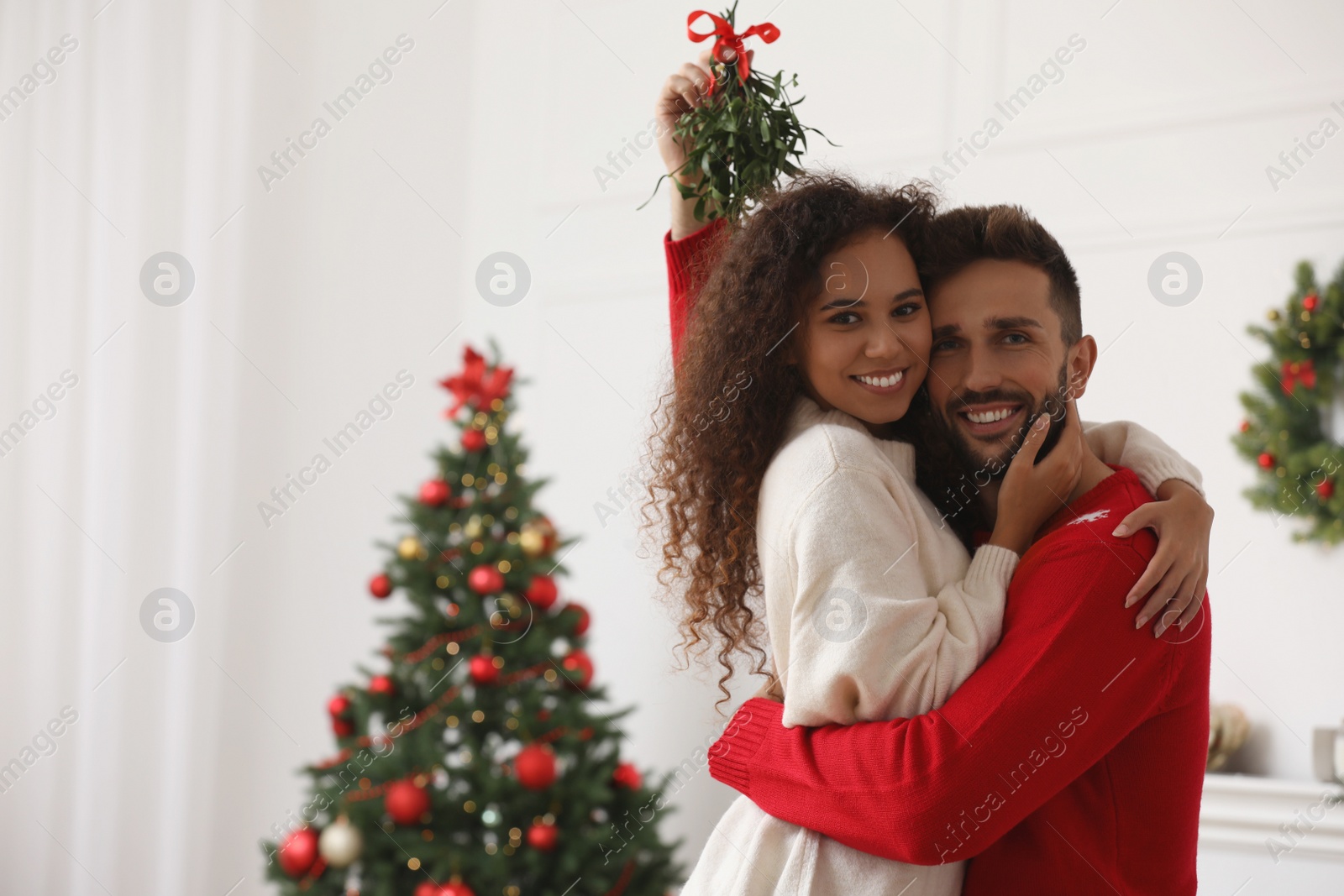 Photo of Portrait of lovely couple under mistletoe bunch in room decorated for Christmas