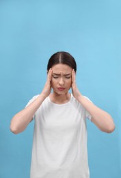 Woman suffering from headache on light blue background. Cold symptoms