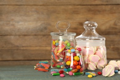 Photo of Jars with different delicious candies on light blue wooden table, space for text
