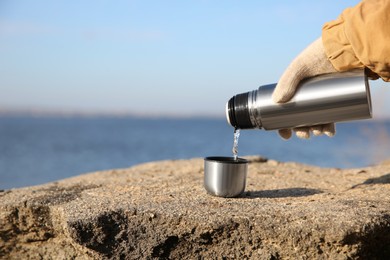 Woman pouring hot drink from thermos bottle into cup outdoors, closeup