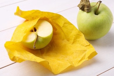 Photo of Half of apple in yellow beeswax food wrap on white wooden table