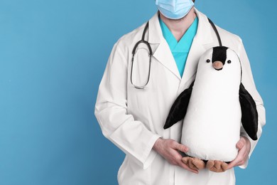 Photo of Pediatrician with toy penguin and stethoscope on light blue background, closeup. Space for text