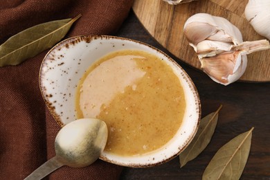Photo of Delicious turkey gravy with bay leaves, garlic and spoon on wooden table, flat lay