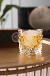 Photo of Alcohol drink with ice cube on golden table in room. Relax at home