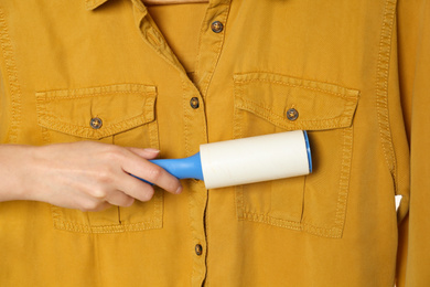 Photo of Woman cleaning yellow shirt with lint roller, closeup