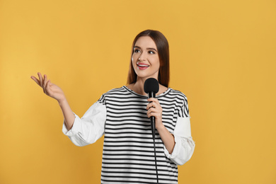 Photo of Young female journalist with microphone on yellow background