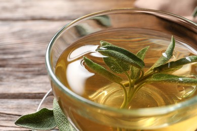 Photo of Cup of aromatic sage tea with fresh leaves on wooden table, closeup