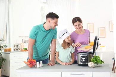 Photo of Happy family preparing food with modern multi cooker in kitchen