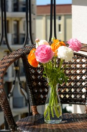 Photo of Bouquet of beautiful bright ranunculus flowers in glass vase on wicker armchair at balcony