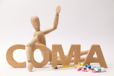 Photo of Word Coma made of wooden letters, human mannequin and pills on light background, closeup