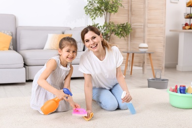 Photo of Housewife with daughter cleaning carpet in room together