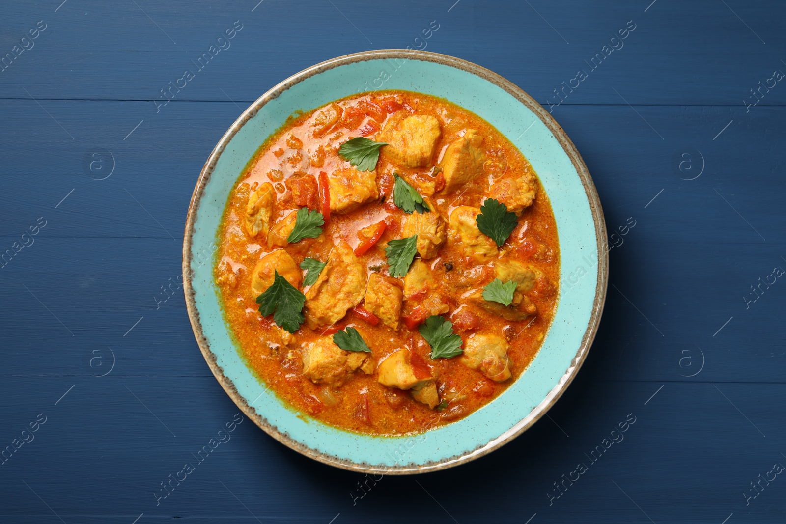 Photo of Delicious chicken curry on blue wooden table, top view