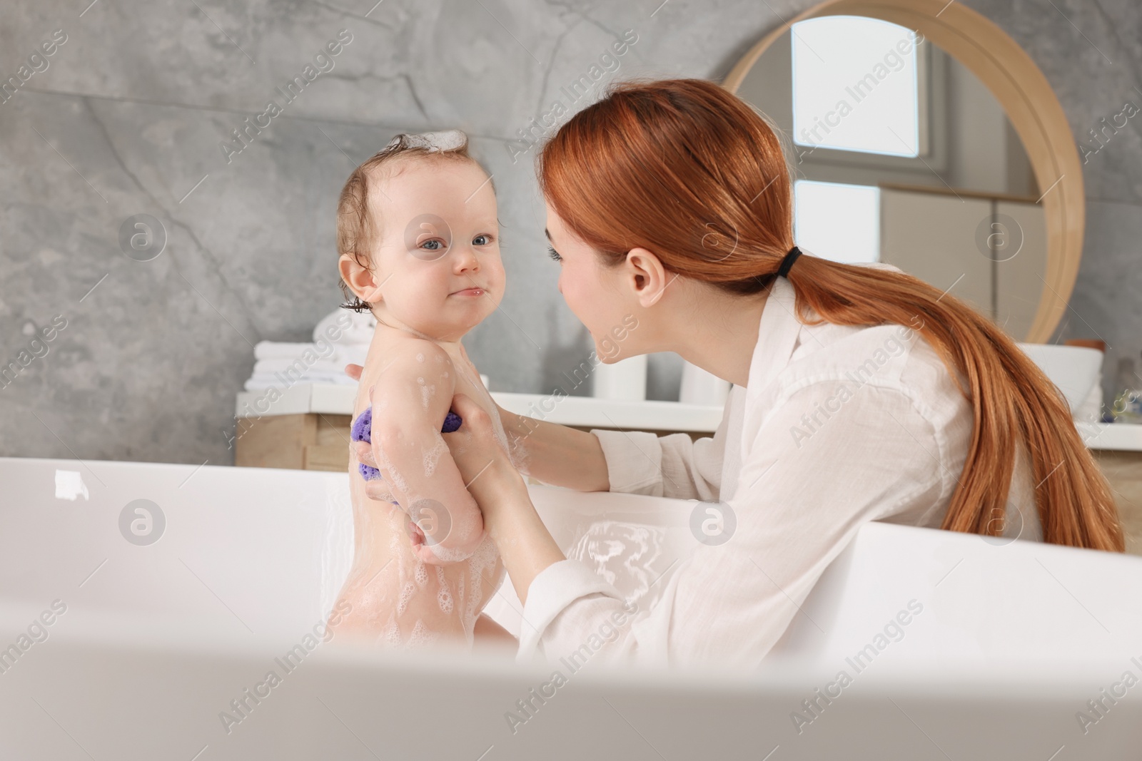 Photo of Mother washing her little baby in tub at home