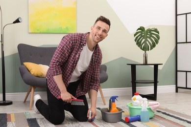 Young man cleaning carpet with brush at home