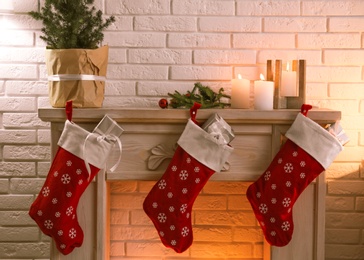 Photo of Red Christmas stockings with gifts on decorative fireplace indoors. Festive interior