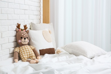 Photo of Toy deer on bed near white brick wall. Children's room interior design