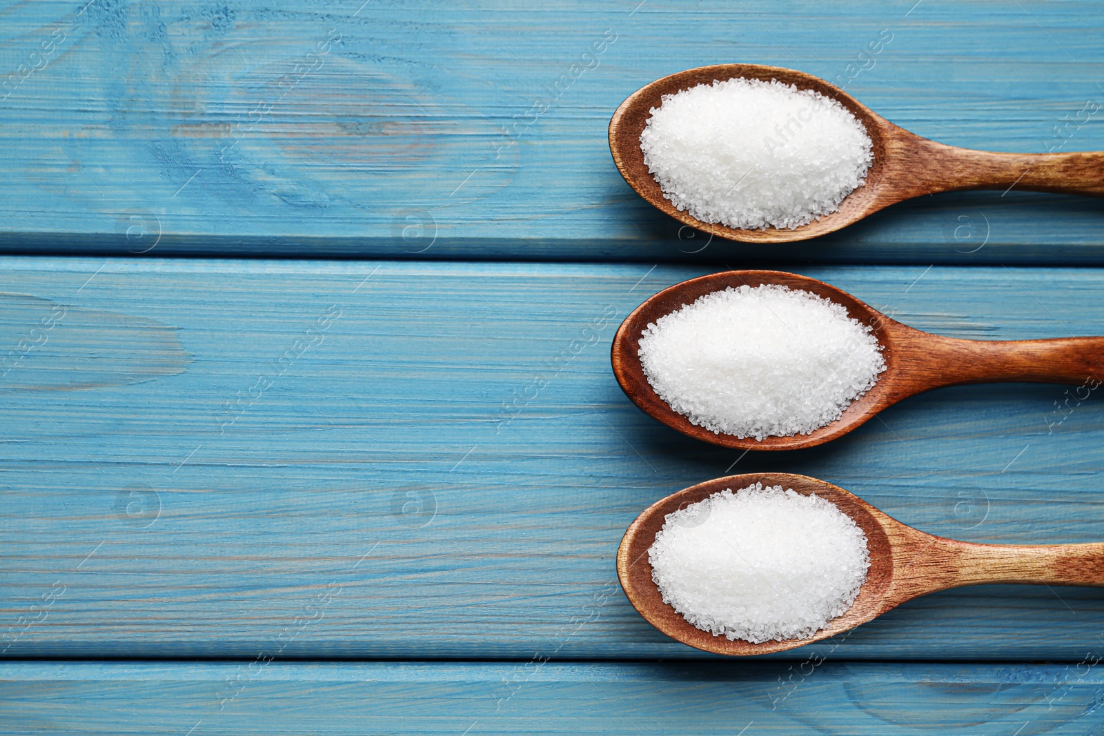 Photo of Granulated sugar in spoons on turquoise wooden table, flat lay. Space for text