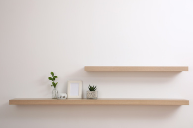 Photo of Wooden shelves with plants and photo frame on light wall