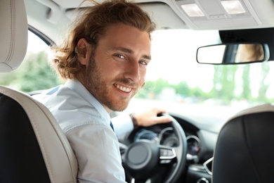 Photo of Attractive young man driving his luxury car, view from backseat