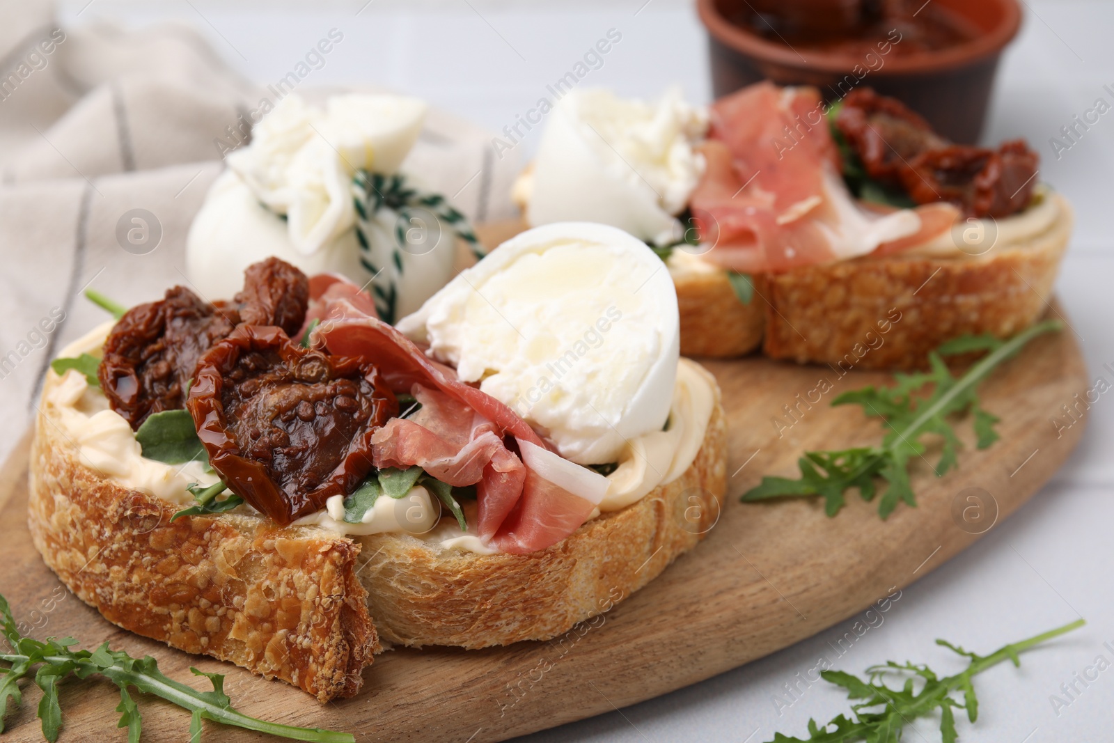 Photo of Delicious sandwiches with burrata cheese, ham and sun-dried tomatoes on white table, closeup