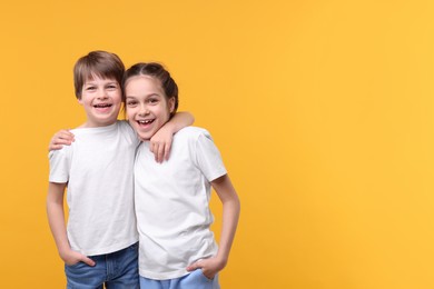 Happy brother and sister on orange background, space for text