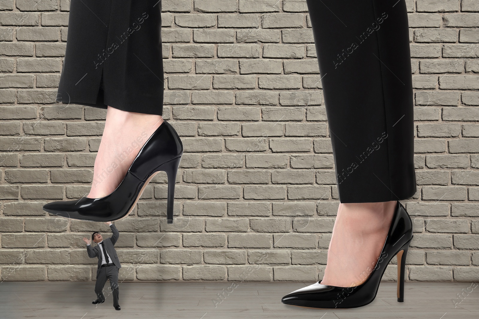 Image of Big woman stepping onto small man near beige brick wall