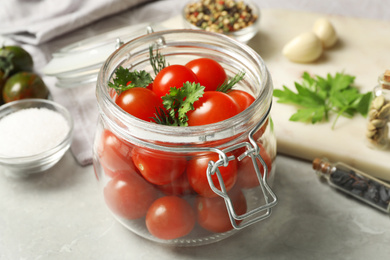 Pickling jar with fresh ripe cherry tomatoes and spices on grey table, closeup