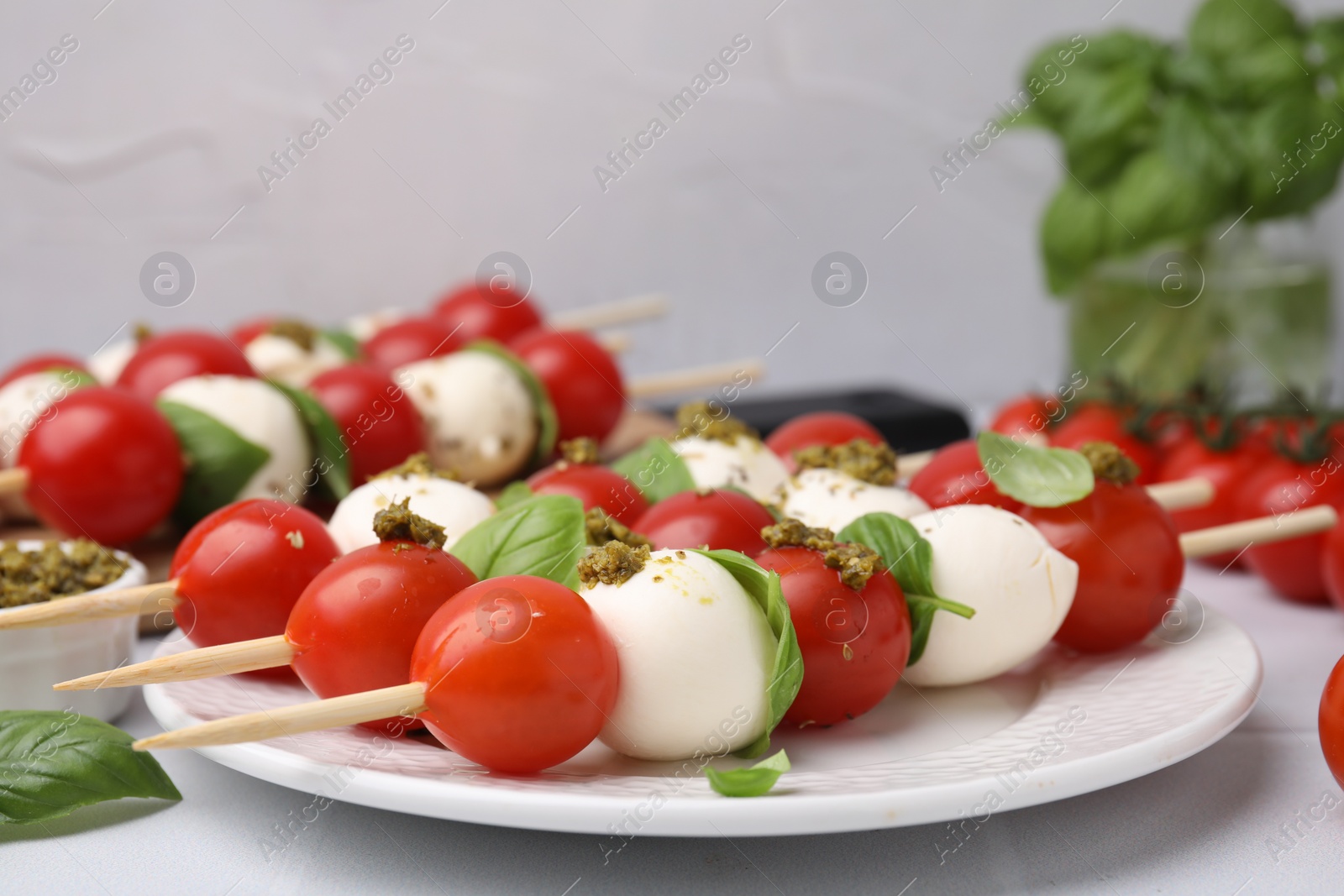 Photo of Caprese skewers with tomatoes, mozzarella balls, basil and pesto sauce on table, closeup. Space for text