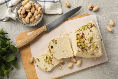 Photo of Tasty halva with pistachios, mint and knife on grey table, flat lay