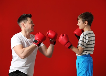 Dad and his son with boxing gloves on color background