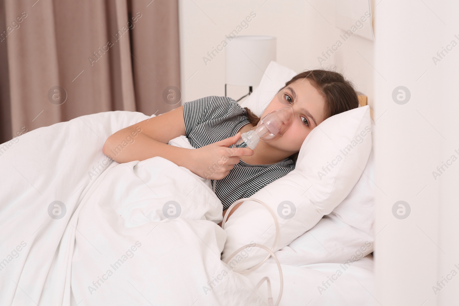 Photo of Cute girl using nebulizer for inhalation on bed at home