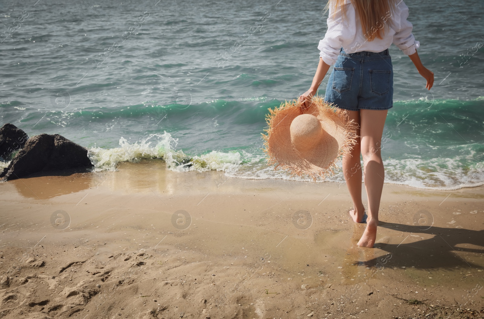 Photo of Young woman with straw hat near sea on sunny day in summer, closeup back view