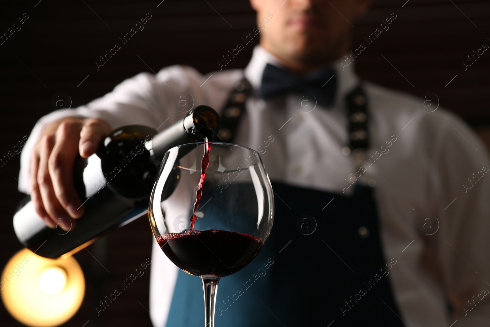 Photo of Bartender pouring red wine into glass indoors, closeup. Low angle view
