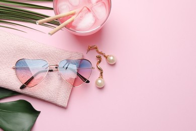 Photo of Heart shaped sunglasses with bag, earrings and glass of drink on pink background, flat lay. Space for text