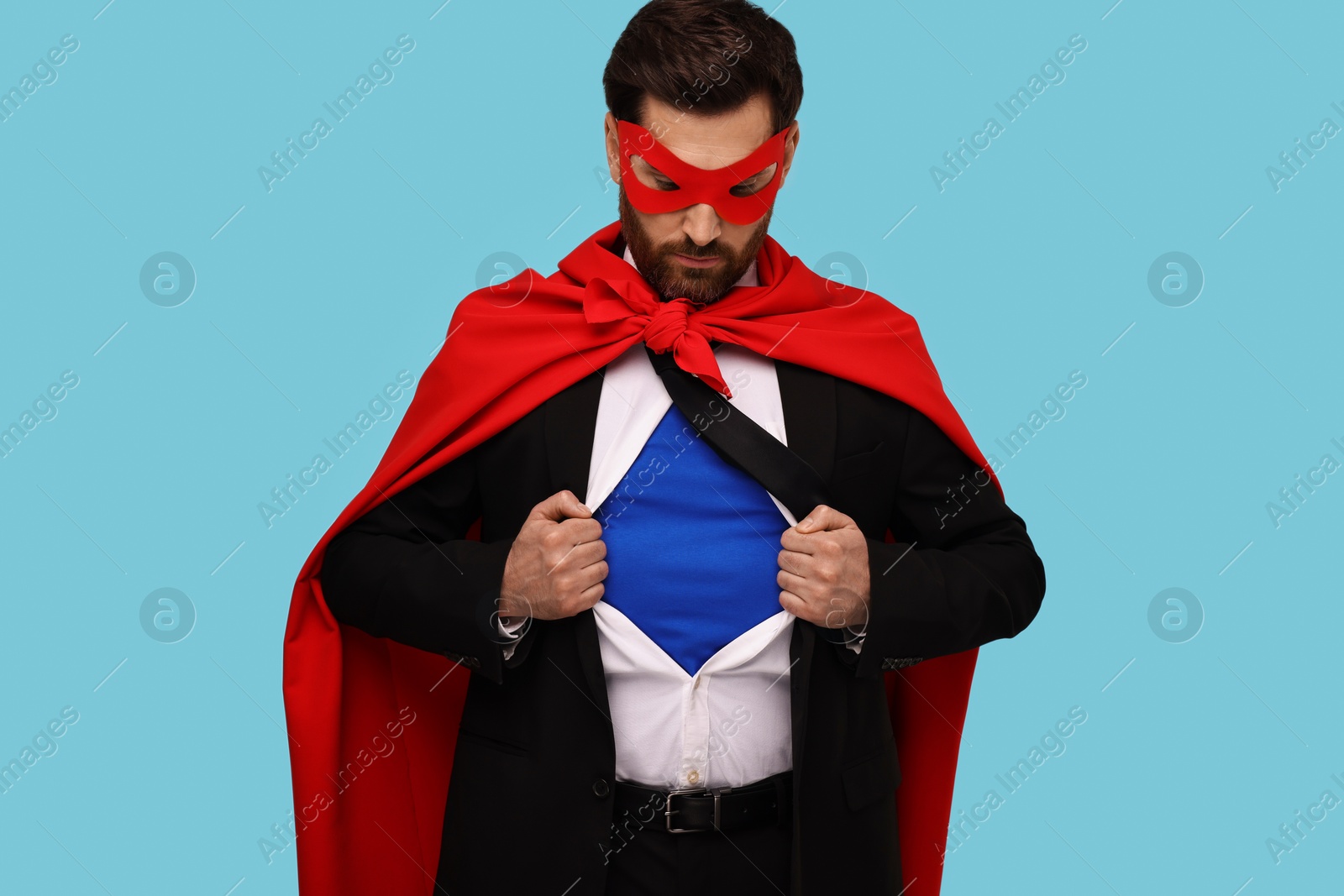 Photo of Confident businessman wearing superhero costume under suit on light blue background