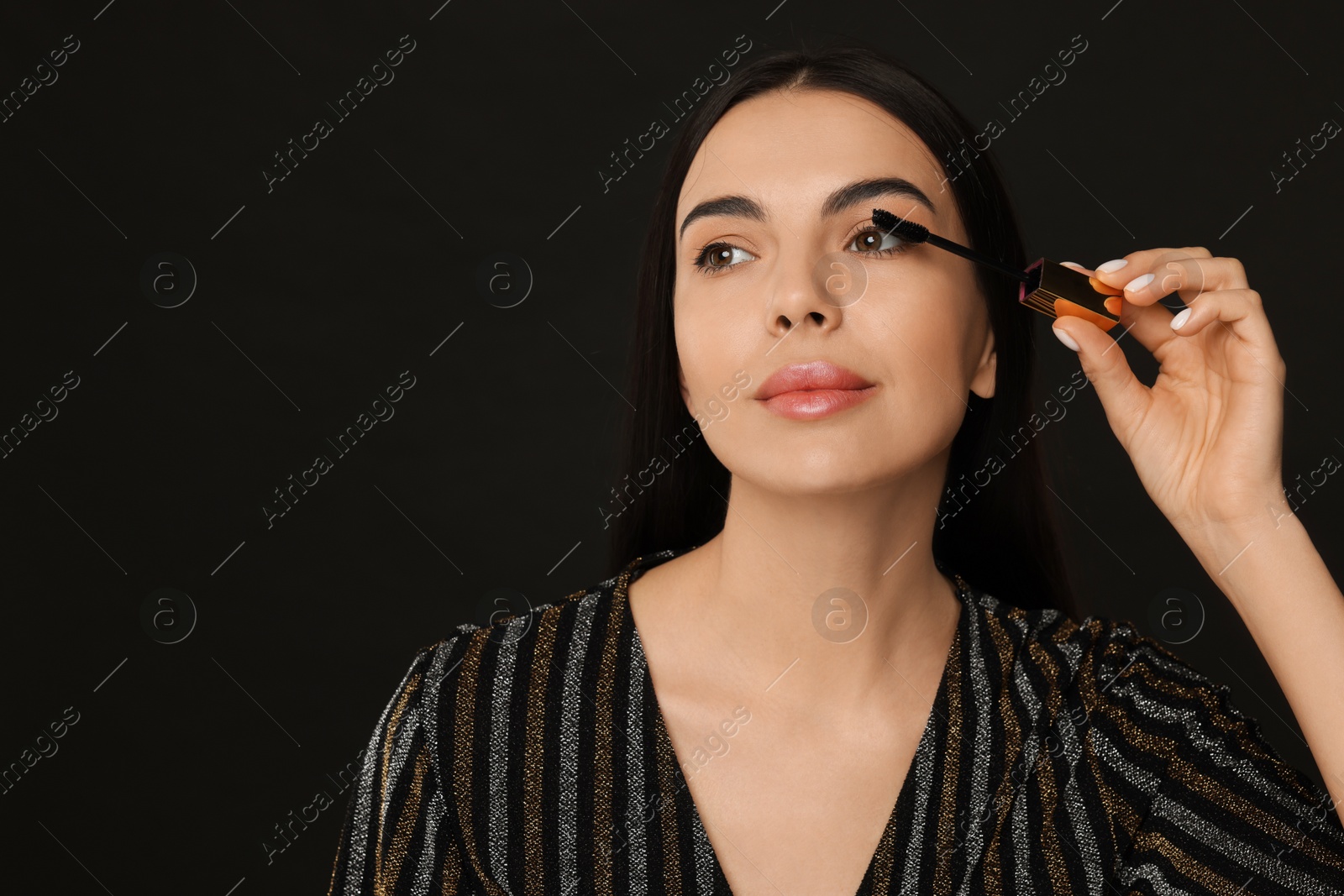 Photo of Beautiful young woman applying mascara on black background, space for text